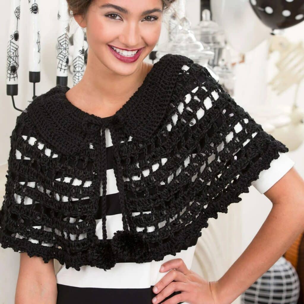 Woman in a short black lacy crochet capelet with a wide collar and pom-pom tie