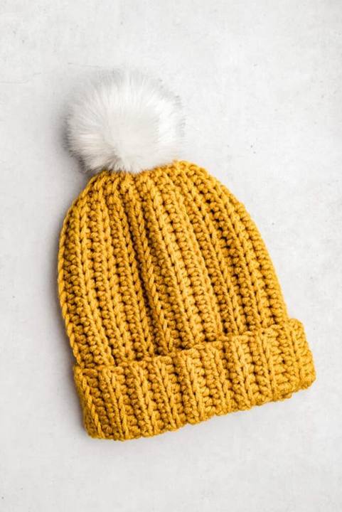 Free crochet beanie pattern for beginners, a mustard ribbed beanie with a folded brim and white pom pom