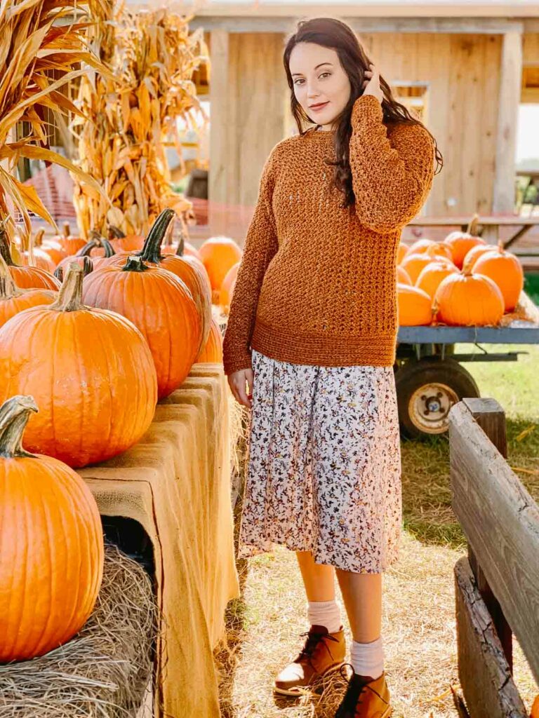 Harvest crochet pullover in rust orange, worn with a floral skirt next to pumpkins
