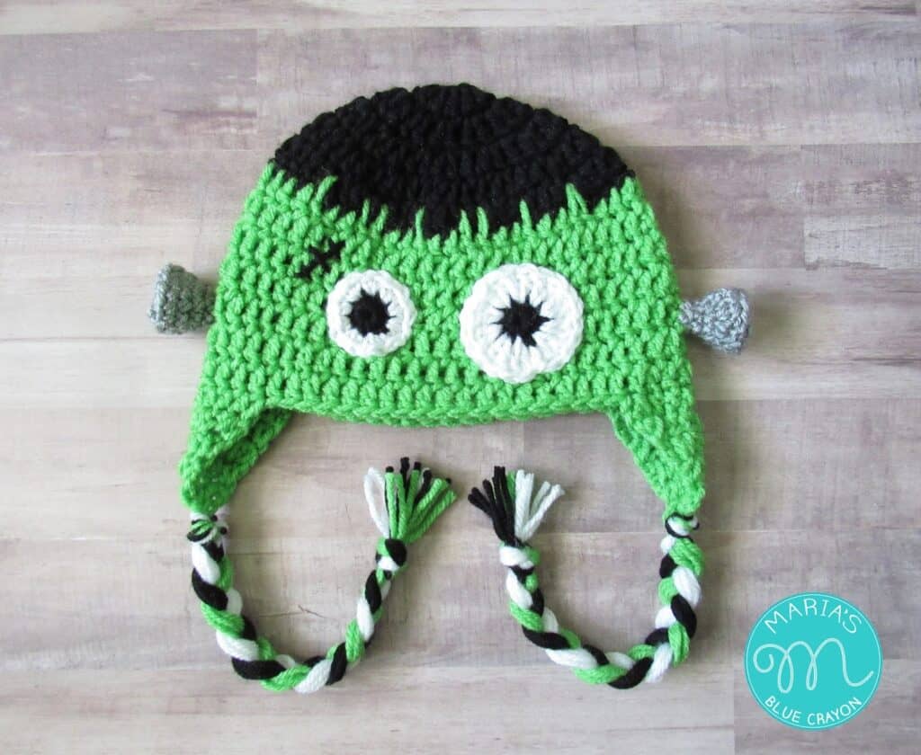 Green crochet Frankenstein hat with black hair, gray bolts and braided earflap tassels