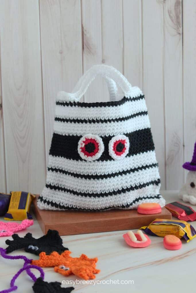 White crochet mummy treat bag with black stripes and red eyes, beginner Halloween pattern