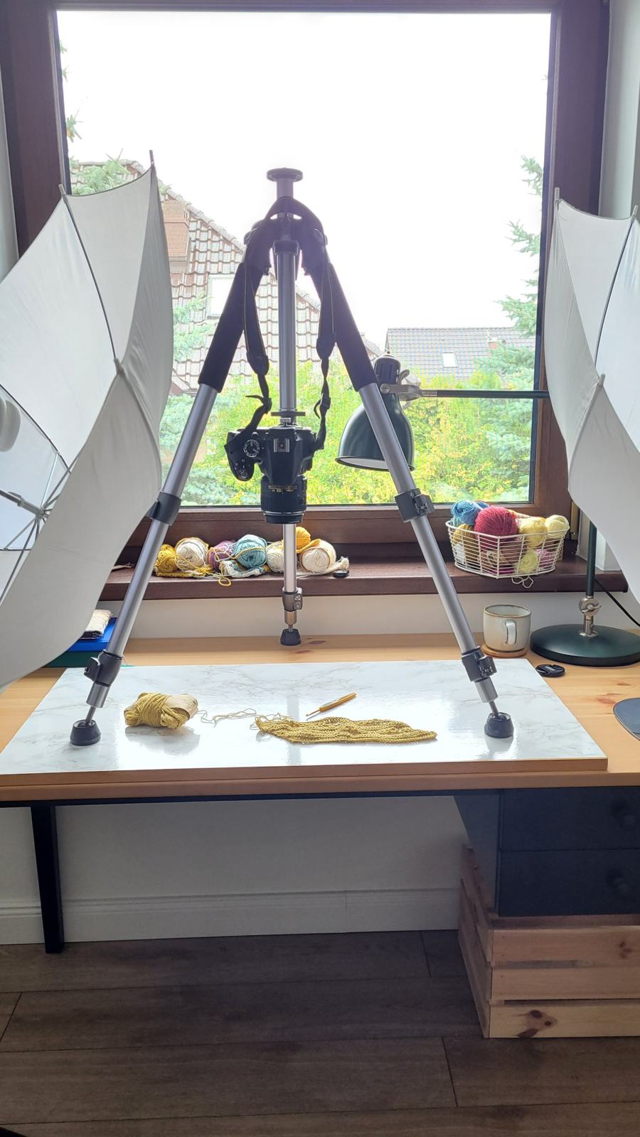 MyCrochetory photo setup with a camera on a tripod, two umbrella lights and baskets of yarn by the window