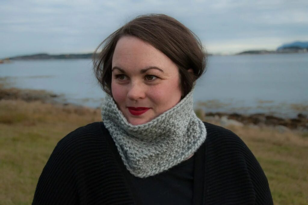 Textured crochet cowl in light gray, worn by a woman by the sea