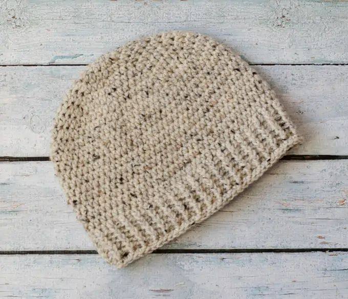 Oatmeal crochet beanie with a ribbed brim lying flat on wood