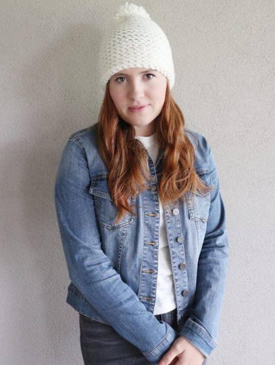 Woman in a denim jacket wearing a white crochet hat with a pom pom