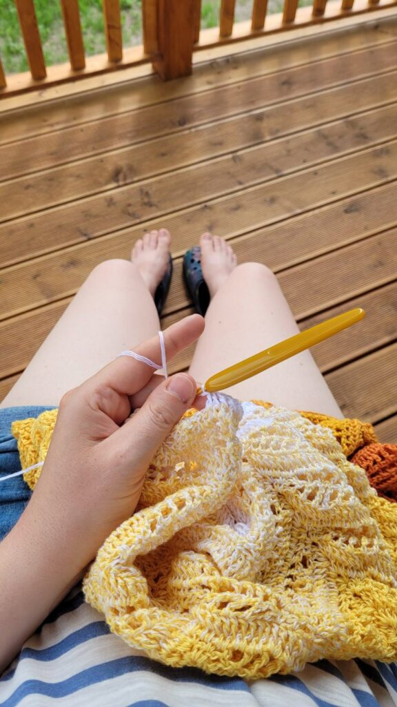 Crocheting a yellow and white lace project on a wooden porch in summer